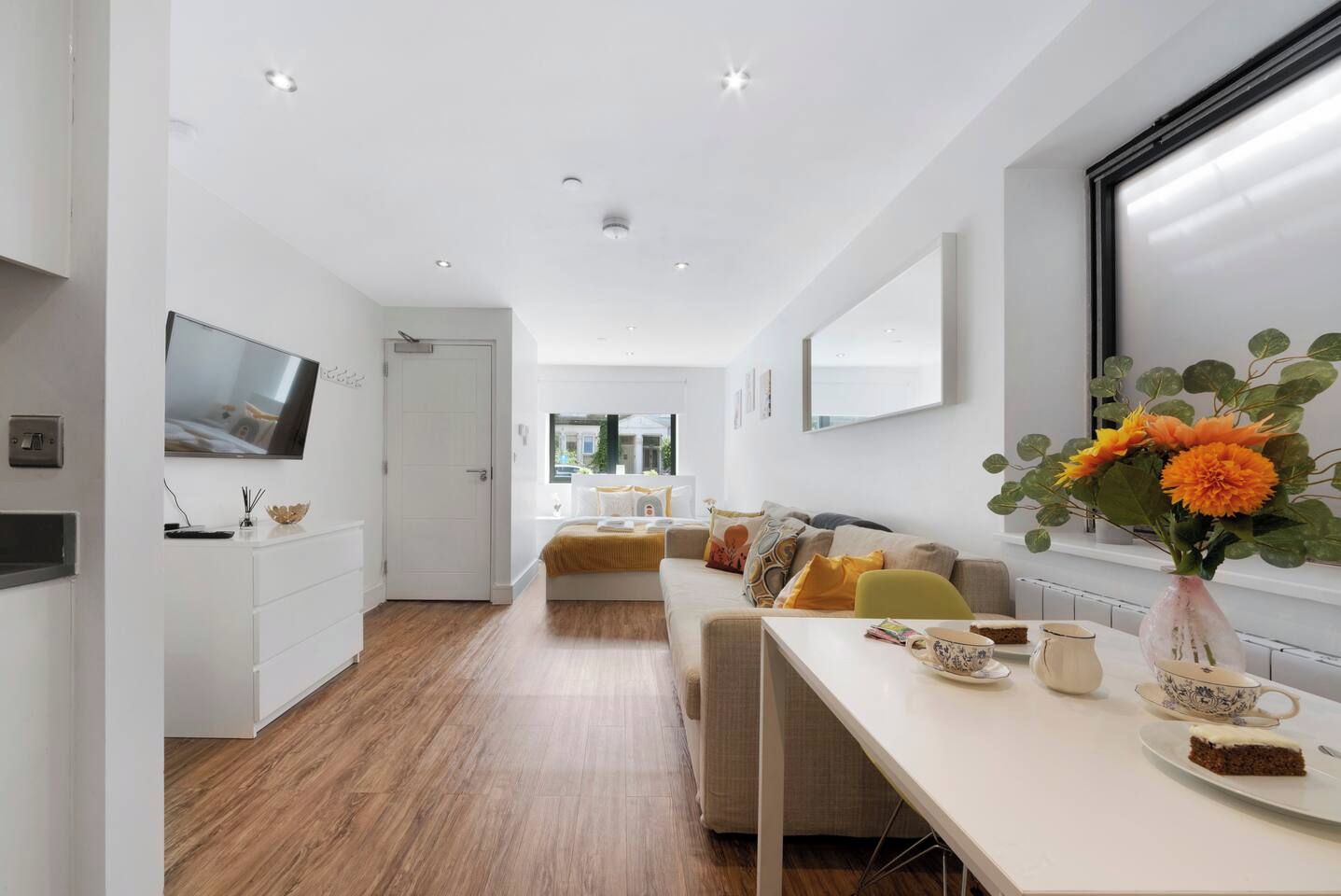 A modern interior with a long dining table, a sofa set, and a TV mounted on the wall.