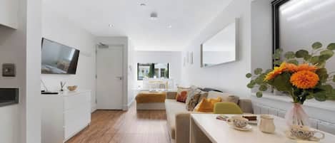 A modern interior with a long dining table, a sofa set, and a TV mounted on the wall.