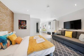 Une chambre d’hôtel moderne avec un lit, un canapé, une télévision et un tableau au mur.
