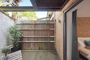 A small outdoor patio area with a wooden fence, a bench, and potted plants.