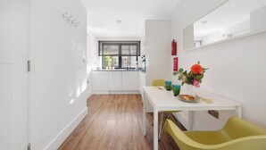 Eine moderne Küche mit weißen Schränken, einem Fenster mit Jalousien, einem Esstisch mit Stühlen und einer Vase mit Blumen.