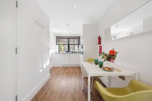 Cozinha moderna com armários brancos, janela com persianas, mesa de jantar com cadeiras e um vaso com flores.