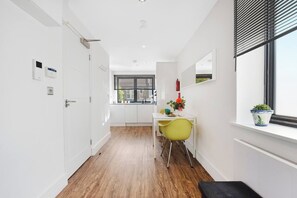 Un couloir étroit avec un plancher en bois, une porte blanche et une fenêtre avec des stores.