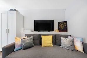 A living room with a grey sofa, a flat-screen TV, a white cabinet, and a painting of sunflowers.