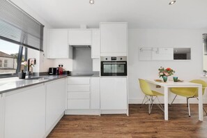 Une cuisine moderne avec des meubles blancs, un four encastré et un coin repas avec des chaises jaunes.
