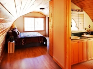 A bedroom with a wooden sloped ceiling, a bed, a small bedside table, and a window. - Eagle's Landings Lakeside Cabin (Lakeside)