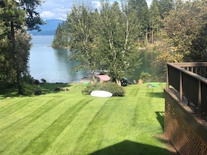 A well-maintained lawn with a white frisbee, a wooden deck, and a lake with trees in the background. - Eagle's Landings Lakeside Cabin (Lakeside)