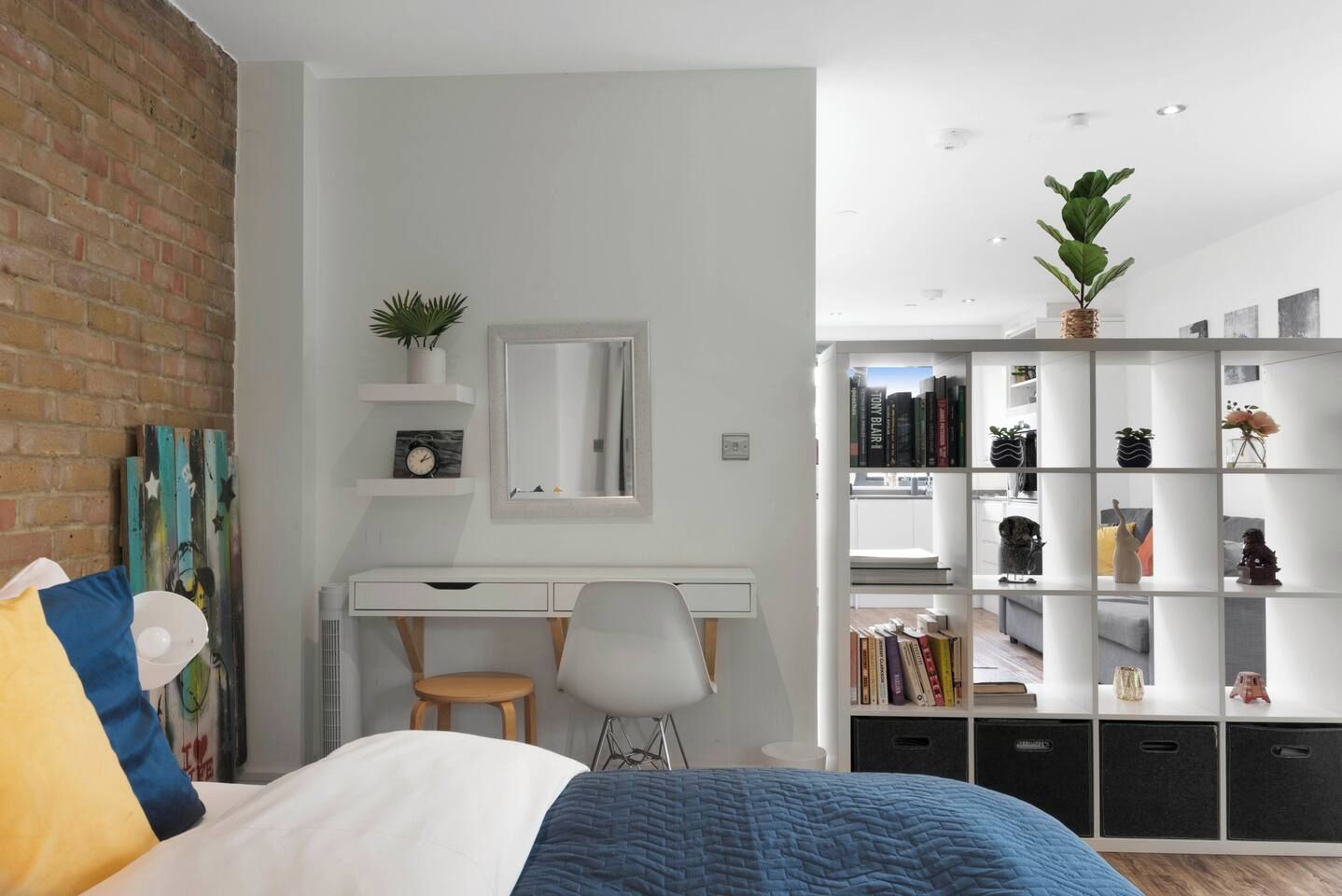 A modern bedroom with a bed, a desk, a chair, a bookshelf, and a mirror.
