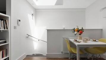 A modern room with a skylight, a dining table with chairs, a radiator, and a bookshelf.