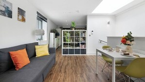 Een moderne woonkamer met een grijze bank, een witte salontafel en een eethoek met een witte tafel en groene stoelen.