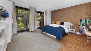 Een moderne slaapkamer met een groot bed, uitzicht op een balkon en een bakstenen muur.