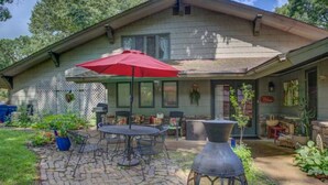 A house with a patio area featuring a round table and chairs, a red umbrella, and a decorative metal planter. - Entire Spacious 4BR Home - close to downtown & minutes to trails! (Bentonville)