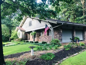 Ein Haus mit Natursteinfassade, einem Steinofen und einem gepflegten Garten mit Vogelbad und einer amerikanischen Flagge.