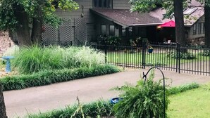 A two-story house with a covered patio, surrounded by a black metal fence and lush greenery. - Entire Spacious 4BR Home - close to downtown & minutes to trails! (Bentonville)