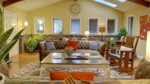 A spacious living room with a high ceiling, stone wall, and a large window. - Entire Spacious 4BR Home - close to downtown & minutes to trails! (Bentonville)