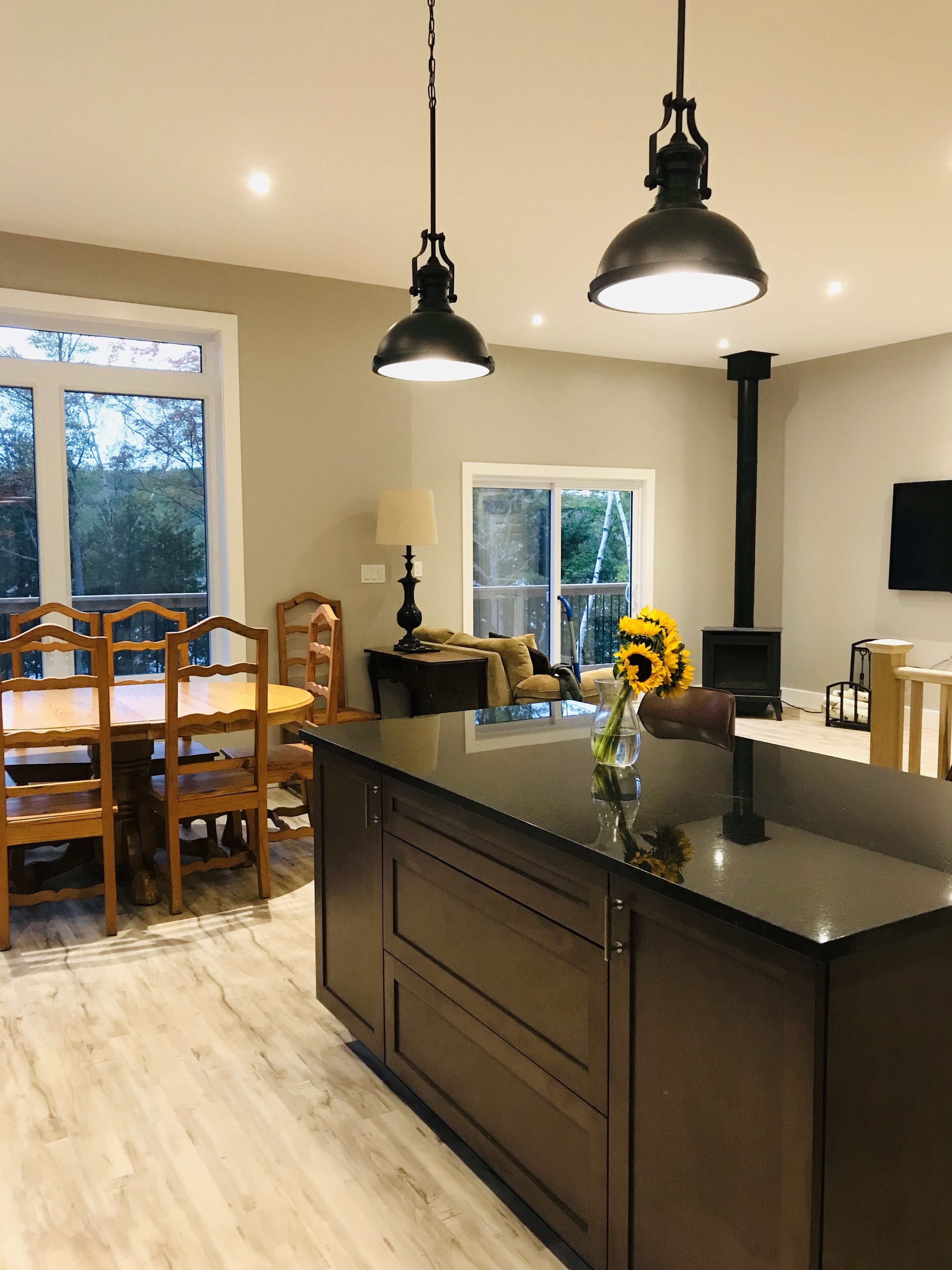 A modern kitchen with a central island, pendant lights, and a dining area with wooden chairs and a table.