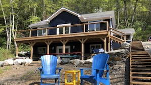 A cabin with a wooden deck, two Adirondack chairs, and a stone pathway leading to the entrance.