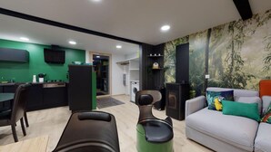 Ein modernes Wohnzimmer mit einer Couch, einem Couchtisch und einem Essbereich mit Tisch und Stühlen. Es gibt eine Küchenzeile mit Kühlschrank und Waschmaschine.