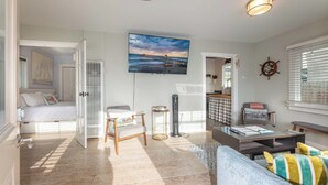 Een goed verlichte woonkamer met een grote televisie, een bank, een salontafel en een bed met uitzicht op het strand.