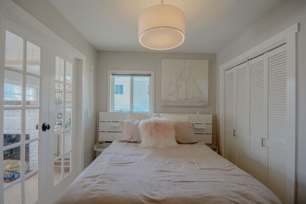 A bedroom with a bed, a window, a door, and a wall-mounted light fixture.