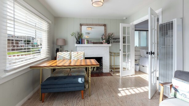 Een kamer met een houten eettafel, een blauwe bank, een witte open haard en een grote spiegel aan de muur.