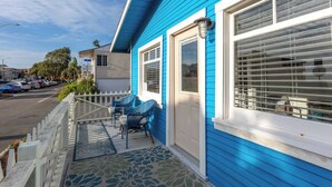 Een blauw huis met een veranda, een witte omheining en uitzicht op de straat.