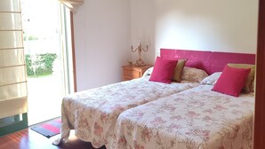 A bedroom with two beds, a nightstand, a lamp, and a window with a curtain.