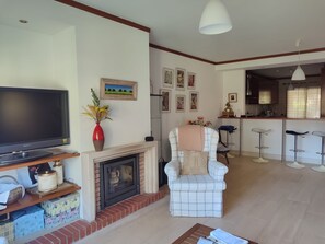 Una sala de estar con televisor, chimenea y un comedor con taburetes de bar.