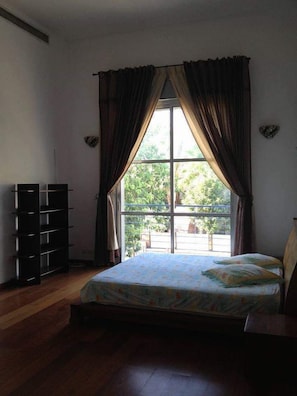A bedroom with a bed, a window with curtains, a bookshelf, and a view of greenery outside. - Casa de la familia (Eilat)