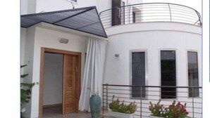 A modern two-story building with a balcony, a wooden door, and a large vase. - Casa de la familia (Eilat)