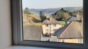 Une vue depuis une fenêtre donnant sur un quartier résidentiel, avec des maisons, une route et des collines au loin.