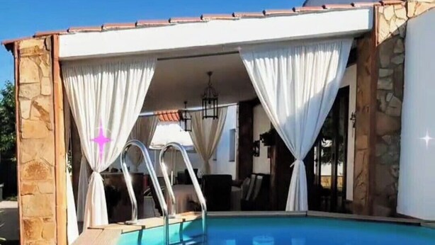 Une piscine dotée d’une terrasse en bois, de murs en pierre et de rideaux blancs.