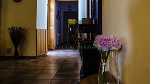 Un couloir avec une porte en bois, une horloge au mur et un vase rempli de fleurs sur une table.