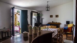 Un coin repas avec une table en bois, des chaises et un lustre. On aperçoit un canapé et un téléviseur au fond.