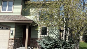 A two-story house with a front porch, a garage, and a tree in the yard.