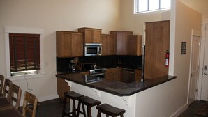 A kitchen with wooden cabinets, a microwave, and a stove. There are three stools and a window with blinds.