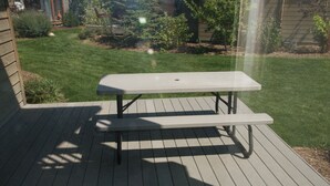 A picnic table on a wooden deck with a grassy yard in the background.
