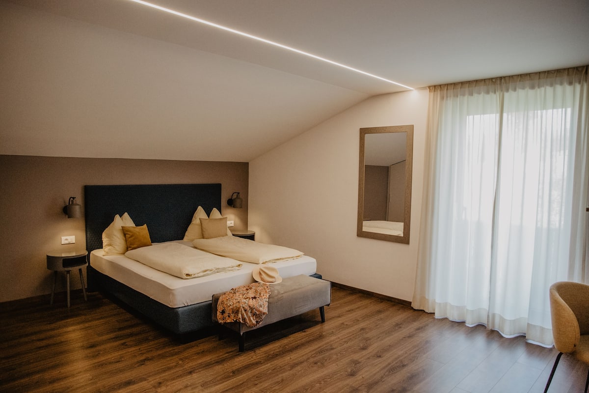 Un dormitorio con una cama grande, mesitas de noche, un espejo y una ventana con cortinas.