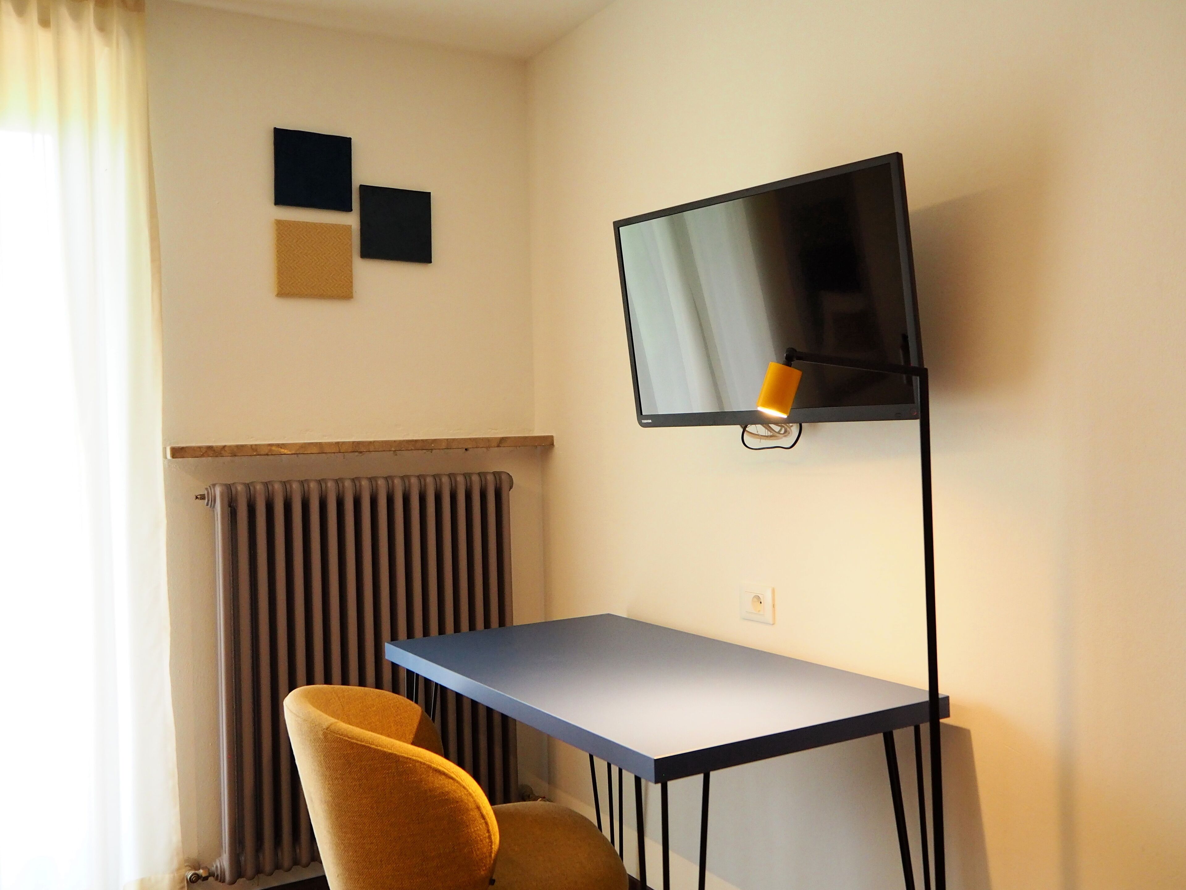 Una habitación con escritorio, una silla, radiador y televisor de pantalla plana montado en la pared.