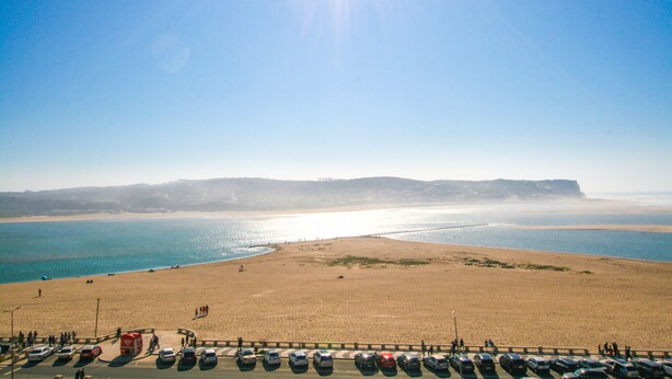 Ein Strand mit einem Parkplatz im Vordergrund und Blick auf das Meer und die Klippen im Hintergrund.