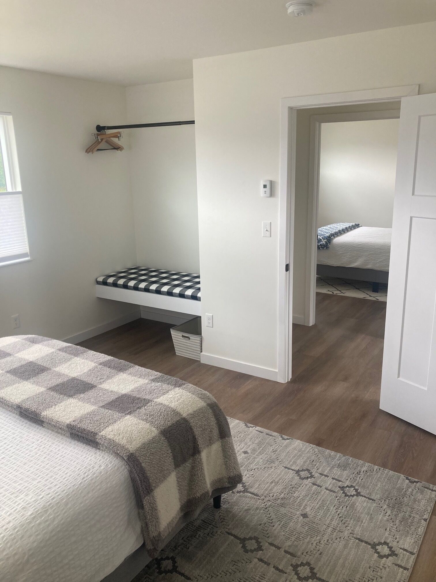 A bedroom with a bed, a bench, a small table, and a door leading to another room.