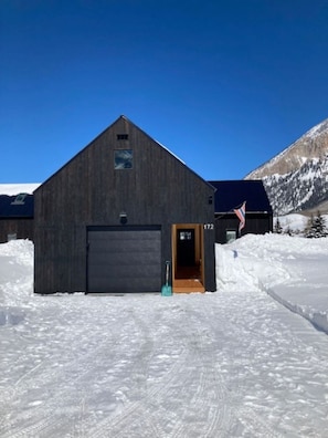 A large, dark wooden building with a garage door, a small entrance, and a flag.