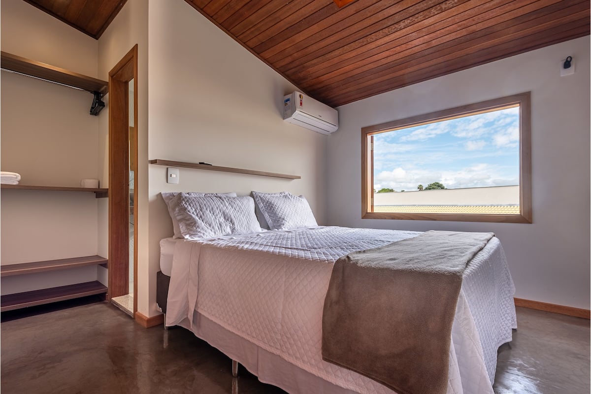 Ein Schlafzimmer mit einem Bett, einem Fenster, einer Holzbalkendecke und einer Wand-Klimaanlage.
