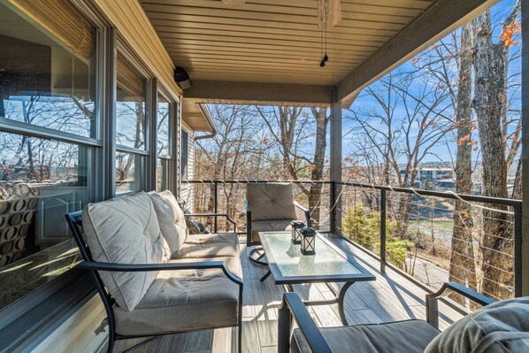 Relax in a serene outdoor space with a comfortable sofa and table, surrounded by trees and a distant view of a body of water.