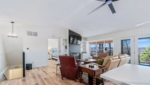 Ampla sala de estar com piso de madeira, mesa de jantar, sofá e uma grande janela com vista para o exterior.