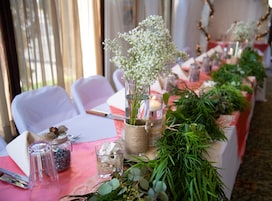 Una mesa decorada con jarrones de vidrio, velas y follaje, probablemente en un comedor o espacio para eventos.