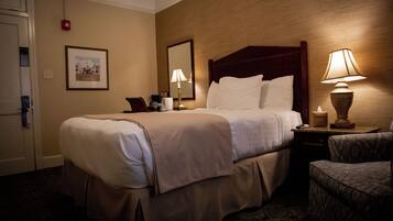 A hotel room with a bed, bedside lamps, a chair, a nightstand, a framed picture on the wall, and a door.
