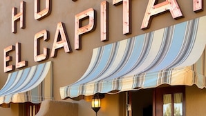 A hotel exterior with a neon sign, outdoor seating with chairs and tables, and a striped awning.