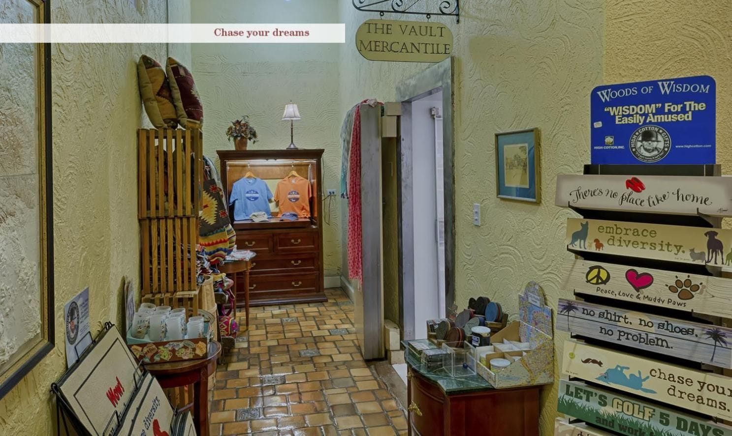 Um corredor com um armário de madeira, uma placa indicando 'THE VAULT MERCANTILE' e uma parede com letreiros motivacionais.