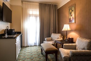 Een hotelkamer met kitchenette, een zithoek, een tafel met lamp en een schilderij aan de muur.